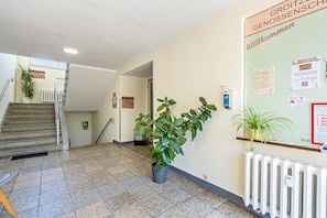 Un couloir avec un escalier, un radiateur et un tableau d’affichage où sont accrochées des annonces.