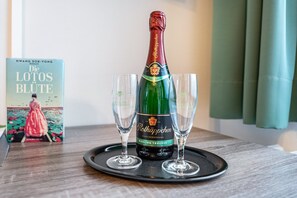 Une bouteille de Rothäppchen Riesling Trocken sur un plateau, accompagnée de deux verres, d’un livre intitulé « Die Lotos Blüte » de Hwang Sok-Yong et d’une fenêtre avec des rideaux.
