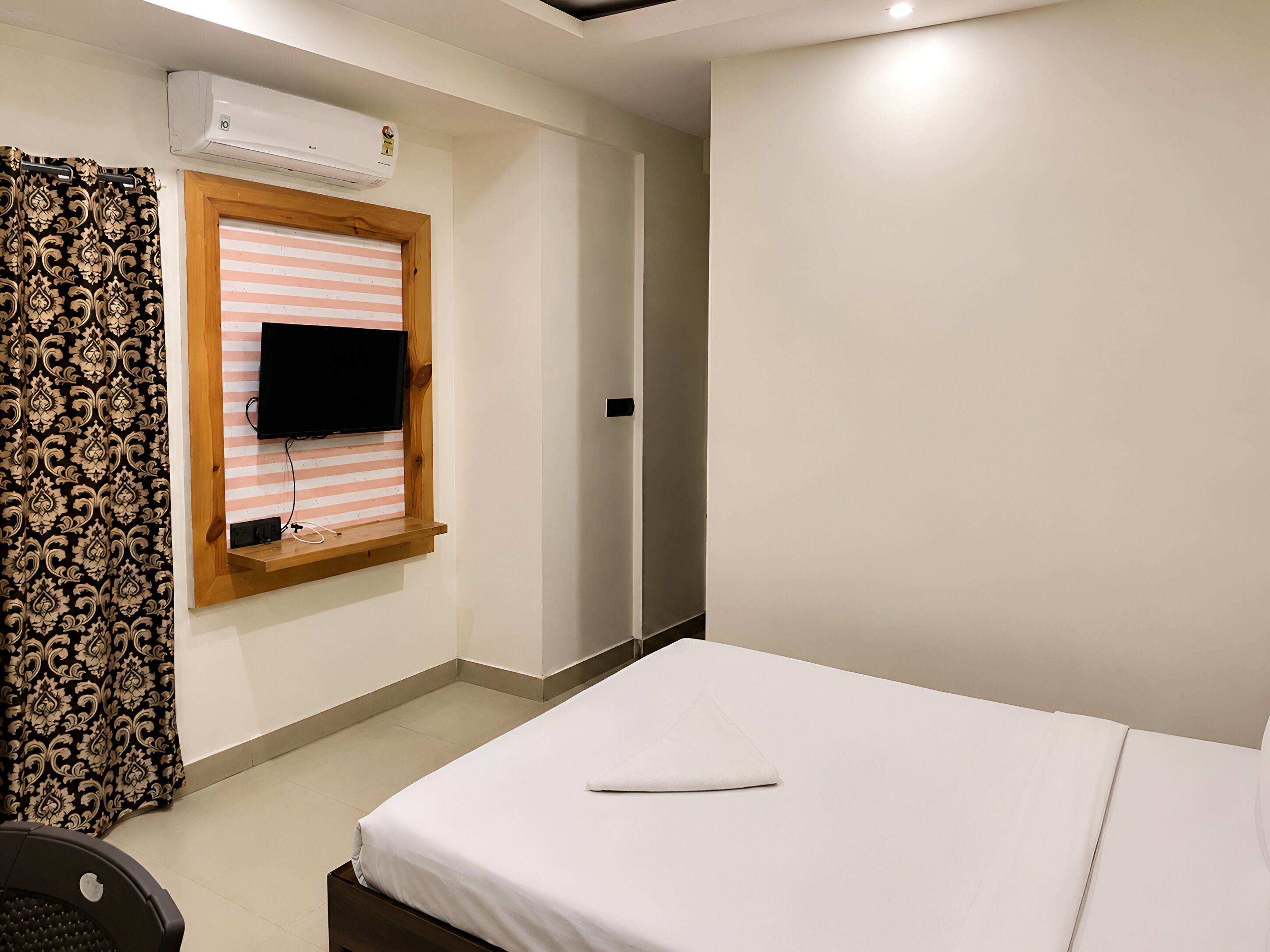 A hotel room with a bed, a television mounted on a wall, an air conditioning unit, and a curtain.