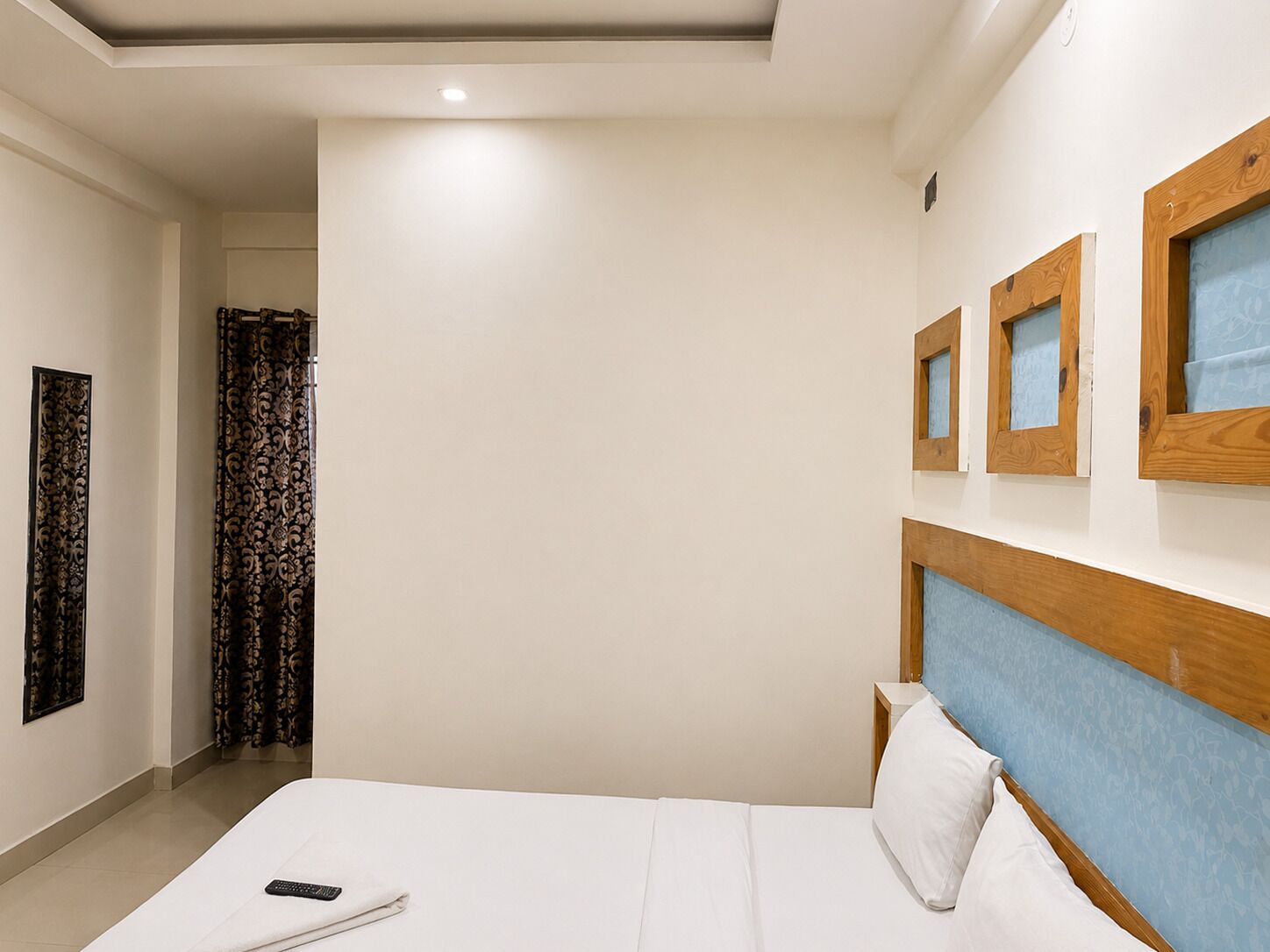 A hotel room with a bed, a nightstand, a wall-mounted TV, and a window with curtains.