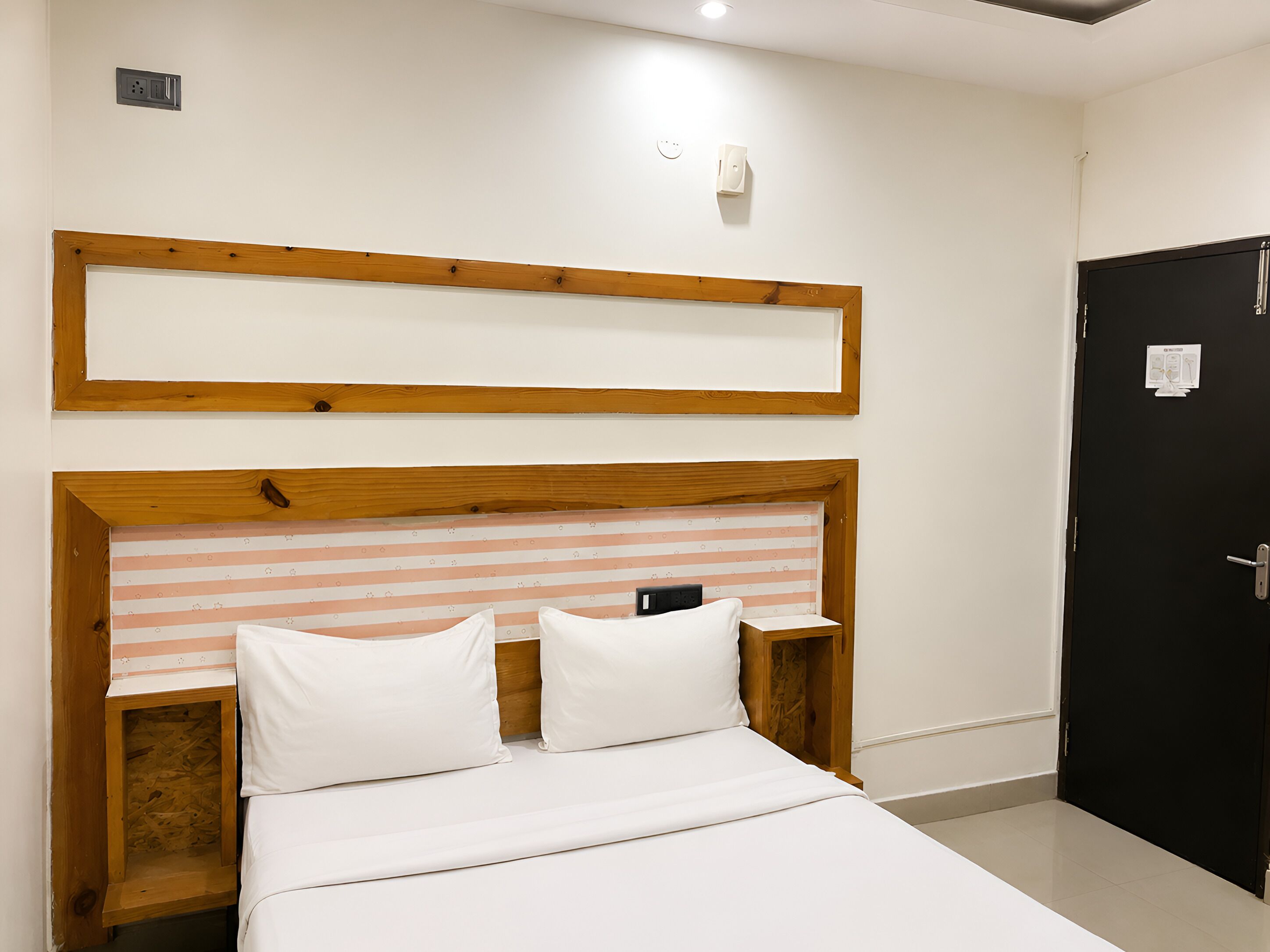 A bedroom with a wooden headboard, a bed with white bedding, a nightstand, and a black door.