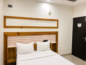 Un dormitorio con cabecera de madera, cama con ropa de cama blanca, mesita de noche y puerta negra.