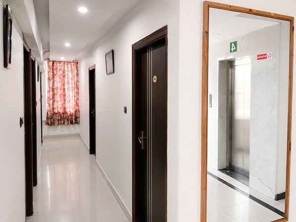 A corridor with doors, a patterned curtain, and a marble floor. - RHG Rooms (Bengaluru)