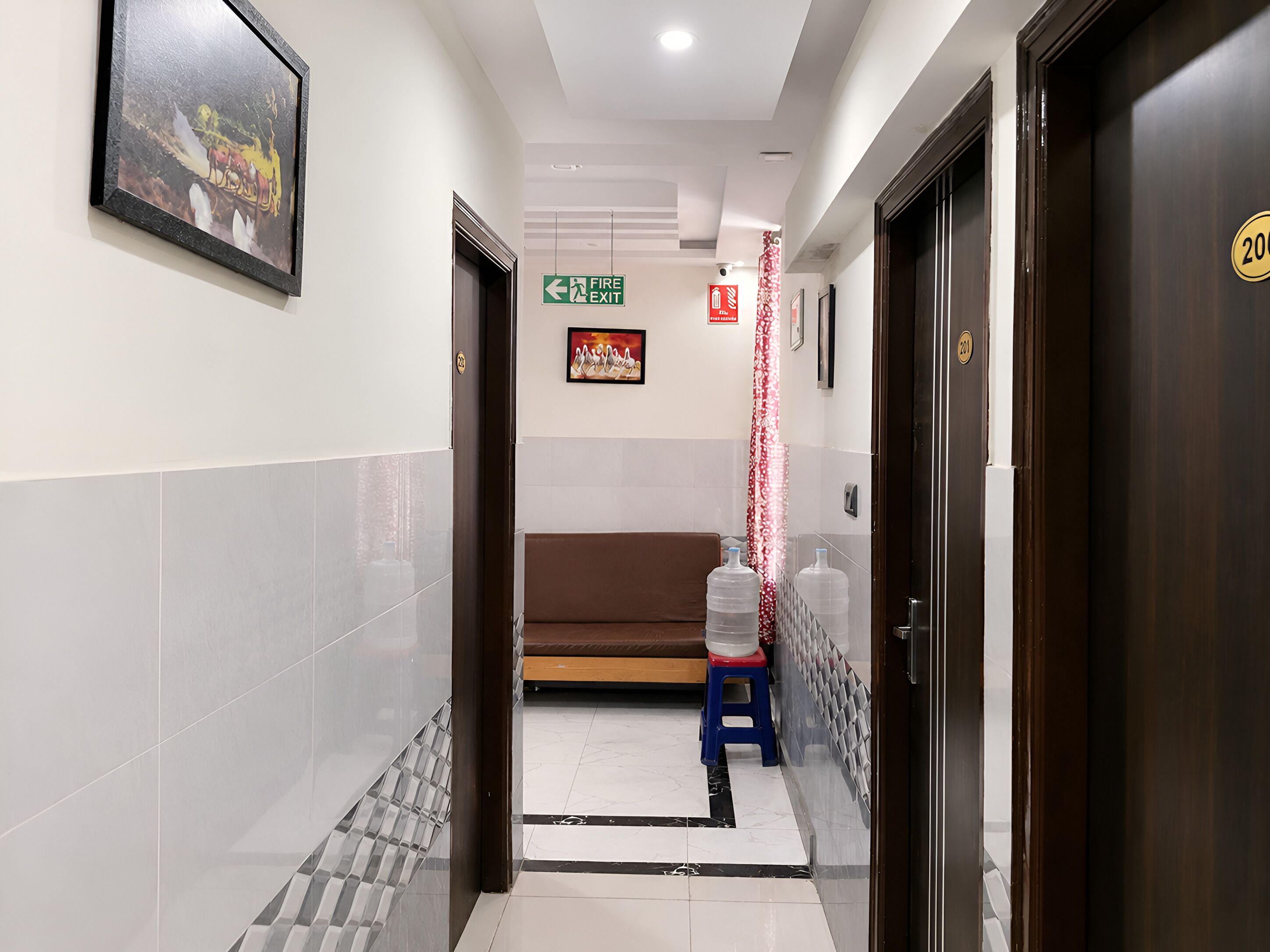 A hotel corridor with a fire exit sign, a bench, and a water dispenser.