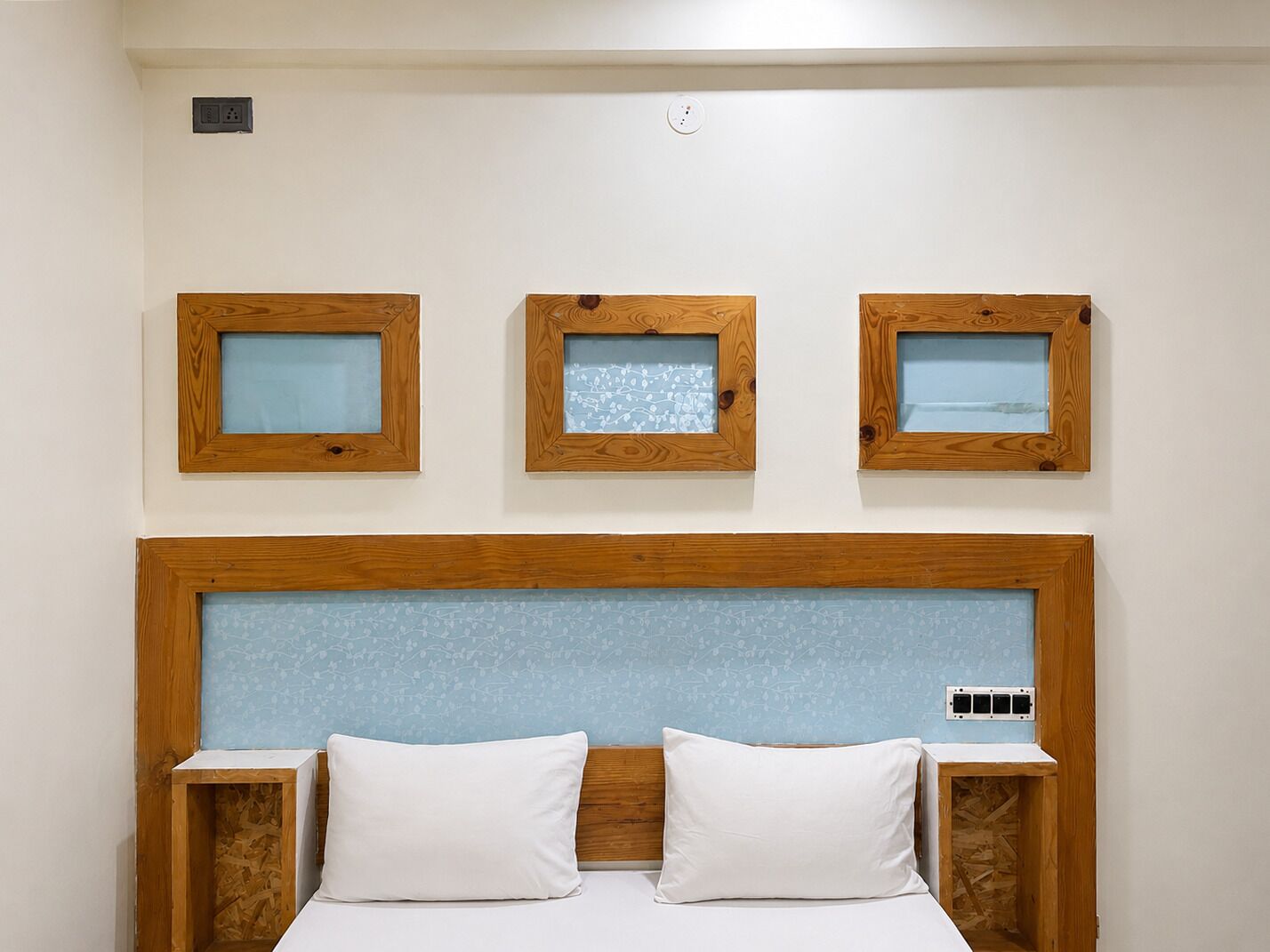 A bedroom with a wooden headboard, two white pillows, and three framed pictures on the wall.