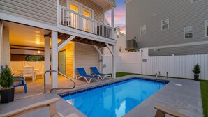 Une piscine avec une terrasse en bois, des chaises longues et un espace patio couvert.