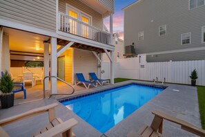 Ein Schwimmbad mit Holzterrasse, Liegestühlen und einer überdachten Terrasse.