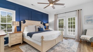 Une chambre dotée d’un grand lit, d’un ventilateur de plafond, d’une table de chevet, d’une chaise et offrant une vue sur l’extérieur grâce à une porte coulissante.