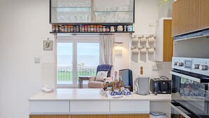 Uma cozinha moderna com forno embutido, cafeteira e vista para o mar através de uma porta de correr de vidro.