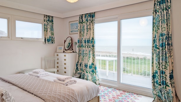 Quarto com cama, penteadeira, espelho e vista para o mar.