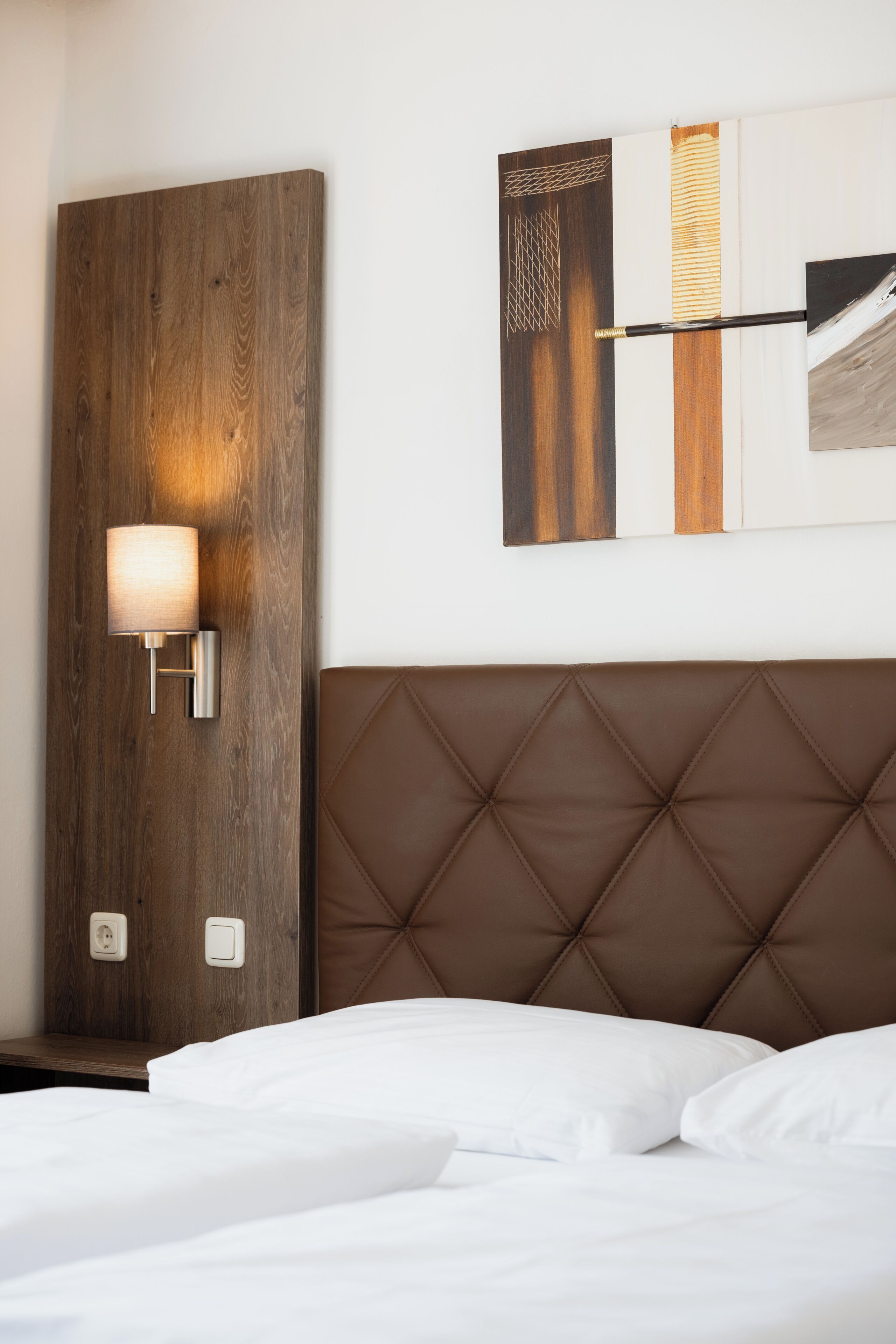 Una habitación de hotel con cabecera de madera, una lámpara de pared y un cuadro sobre la cama.