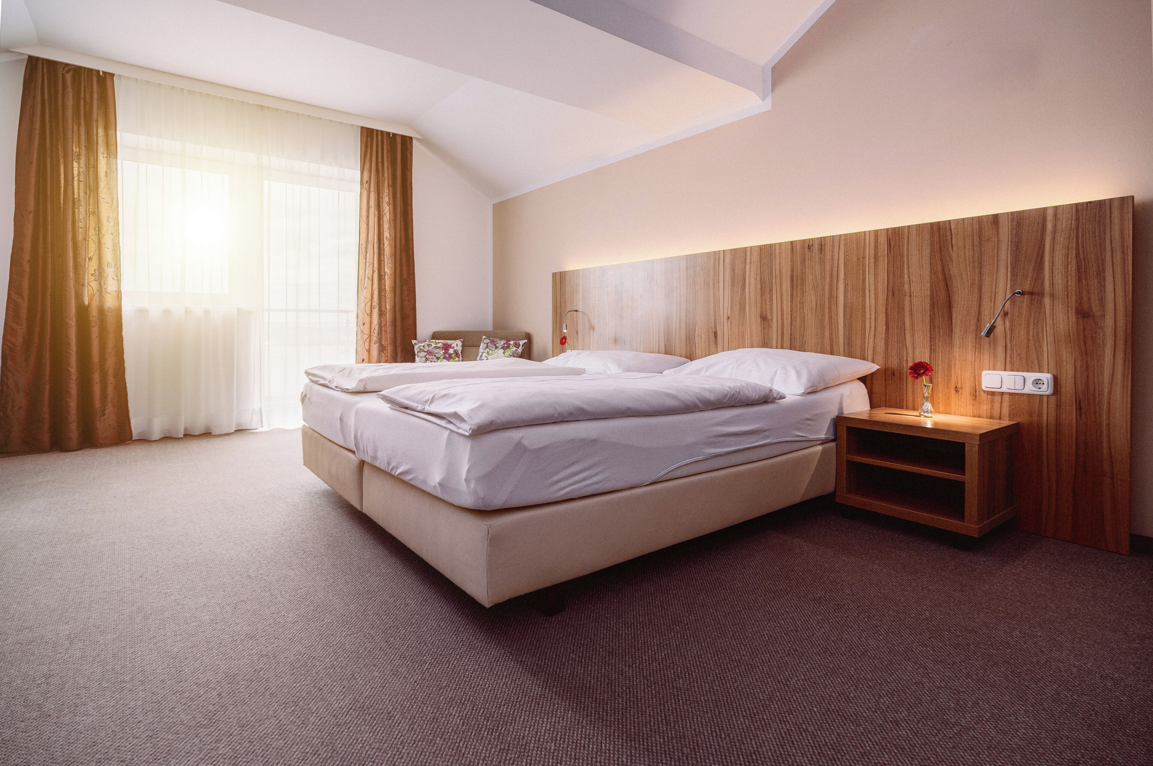 Habitación de hotel moderna con una cama grande, cabecera de madera, mesita de noche con lámpara y vistas al exterior.
