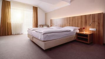Habitación de hotel moderna con una cama grande, cabecera de madera, mesita de noche con lámpara y vistas al exterior.