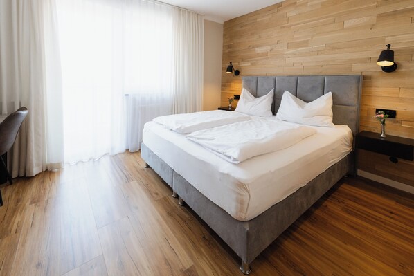 A modern hotel room with a large bed, wooden flooring, and a wooden wall panel. - Hotel Berghof Baumgartner (Obernberg am Inn)
