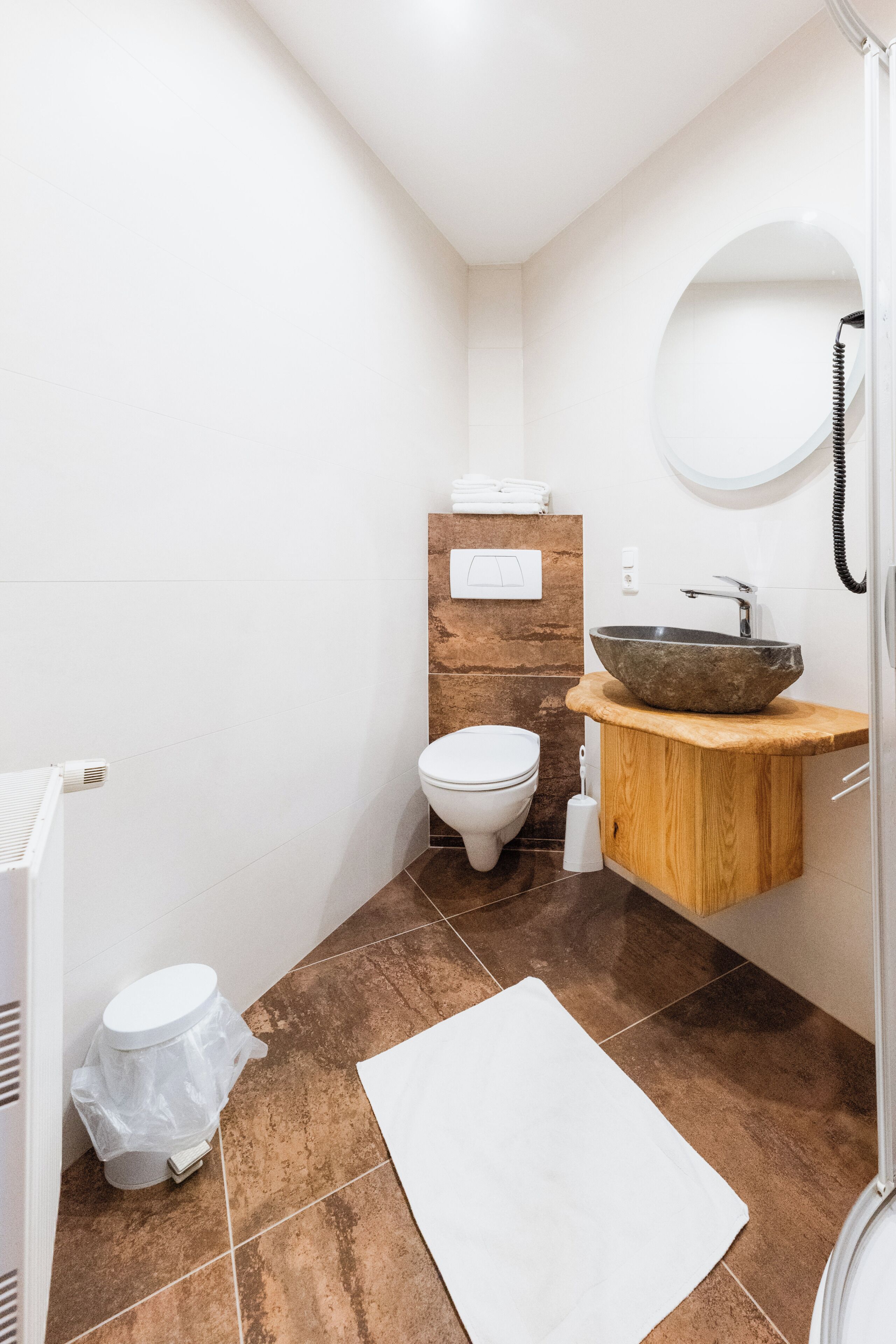 A bathroom with a white toilet, a wooden vanity with a stone basin, a white sink, and a mirror.