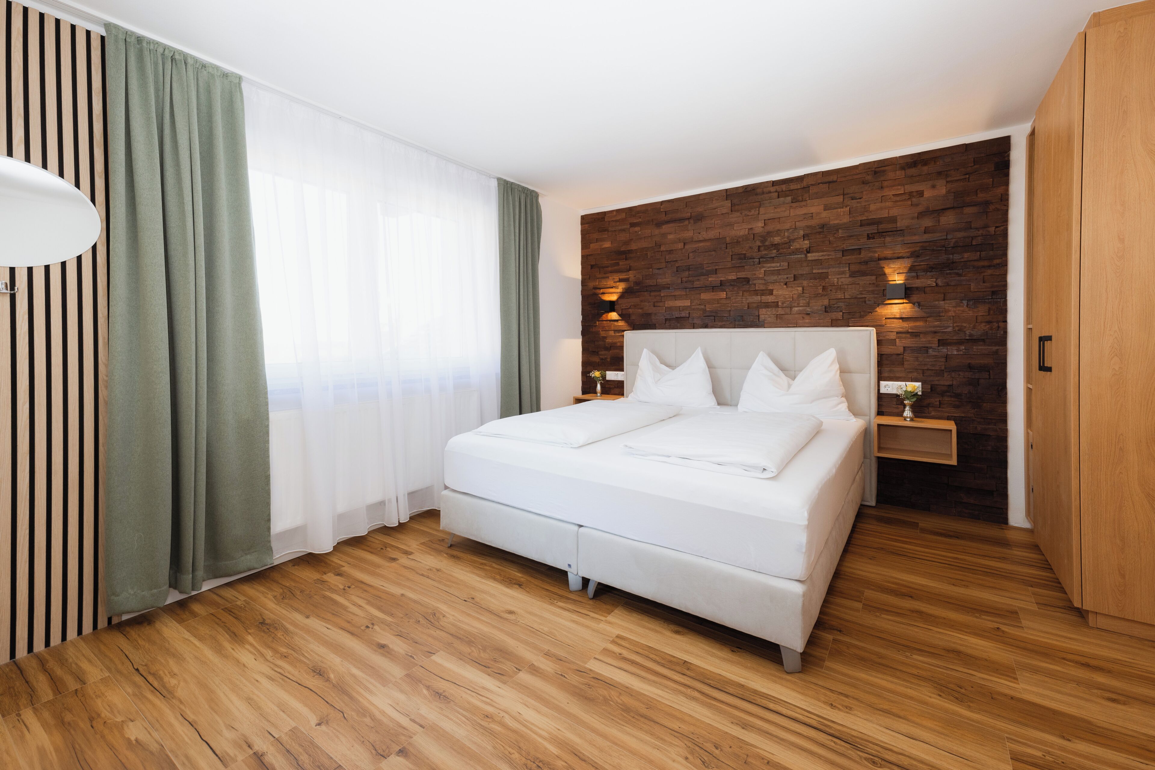 A modern bedroom with a wooden floor, a white bed, a brick accent wall, and two bedside lamps.