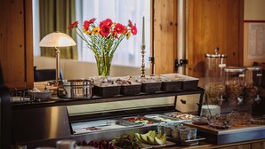 A buffet setup with various food items, a vase of flowers, and a lamp. - Hotel Berghof Baumgartner (Obernberg am Inn)
