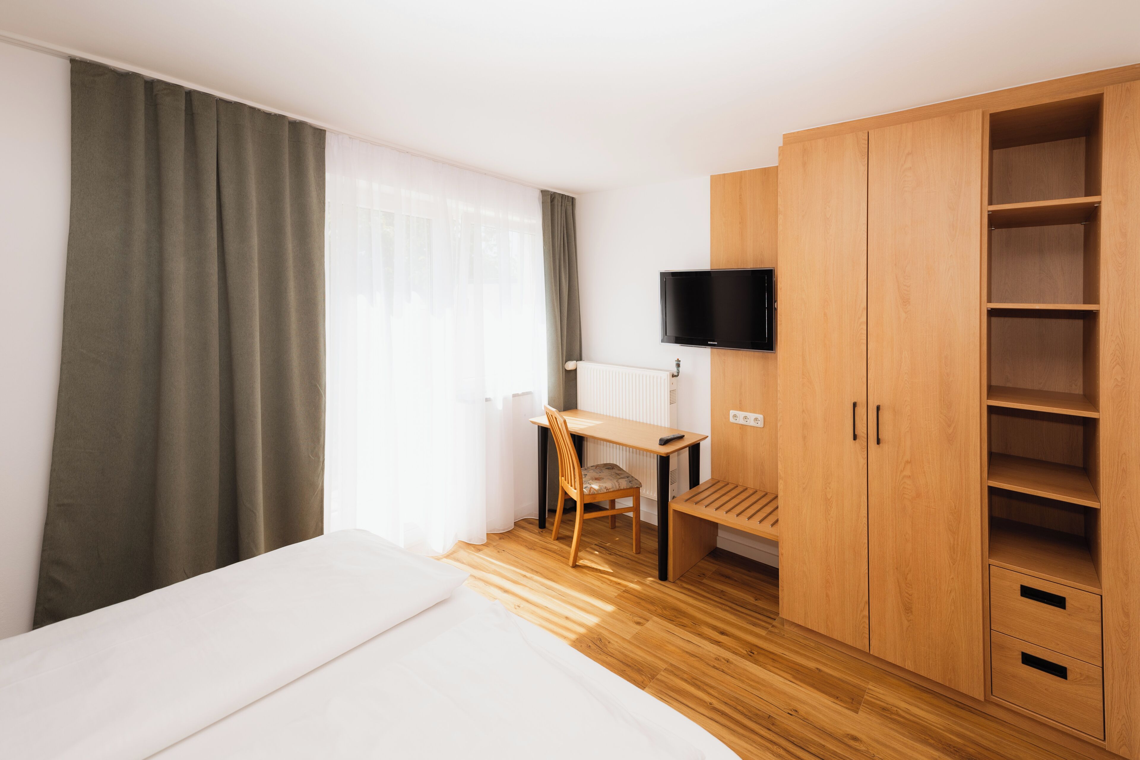 Una habitación de hotel con cama, escritorio, silla, televisor y armario.