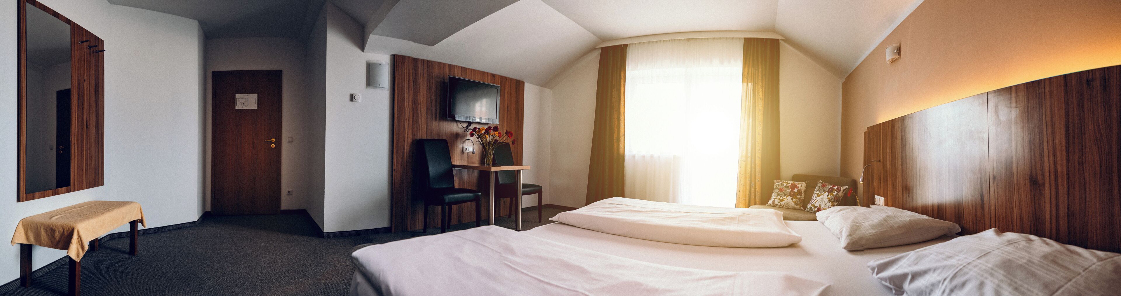 Een hotelkamer met een bed, een bureau, een stoel, een televisie en een raam met gordijnen.