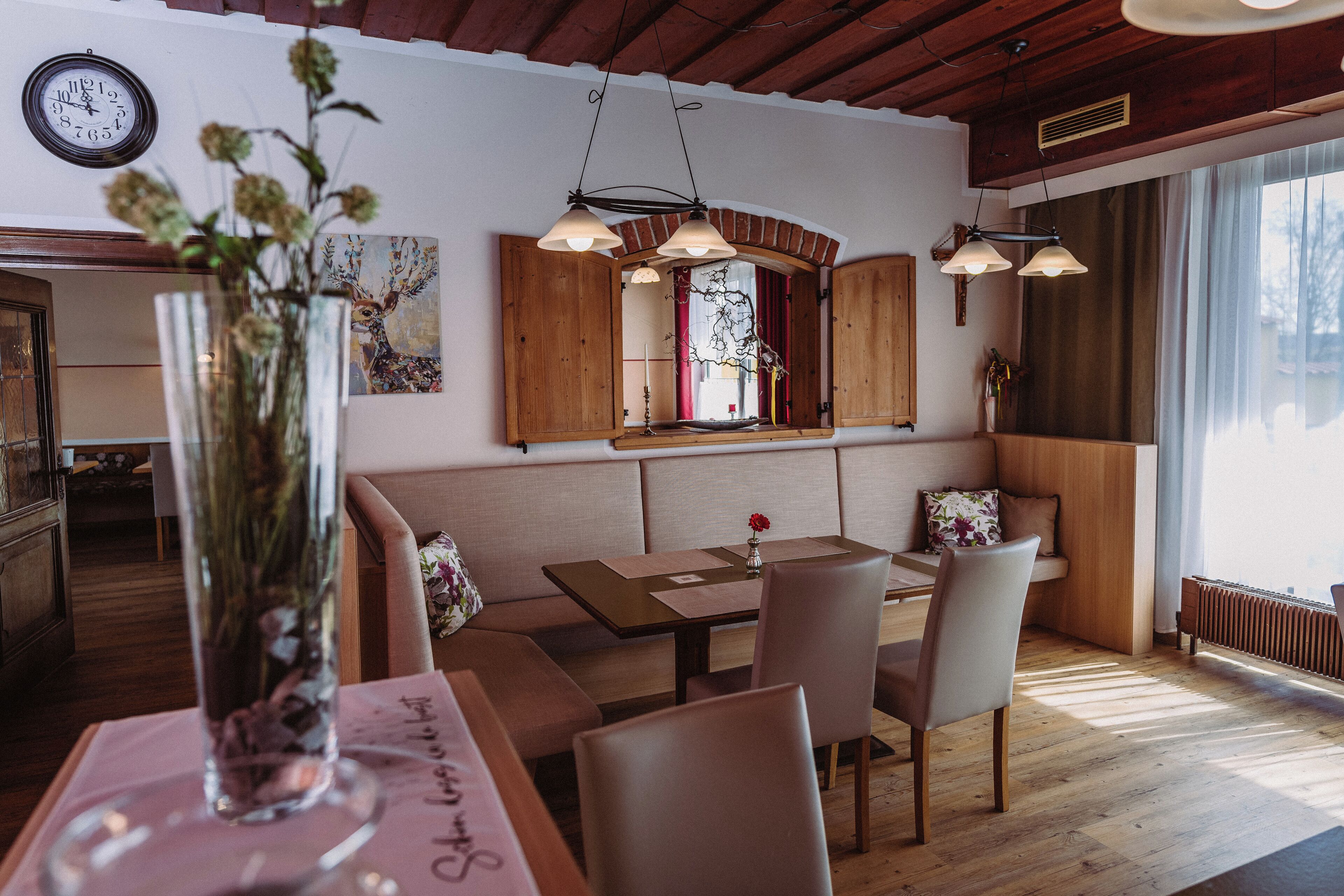 Un comedor con una mesa de madera, sillas, un jarrón con flores, un reloj y una ventana con cortinas.