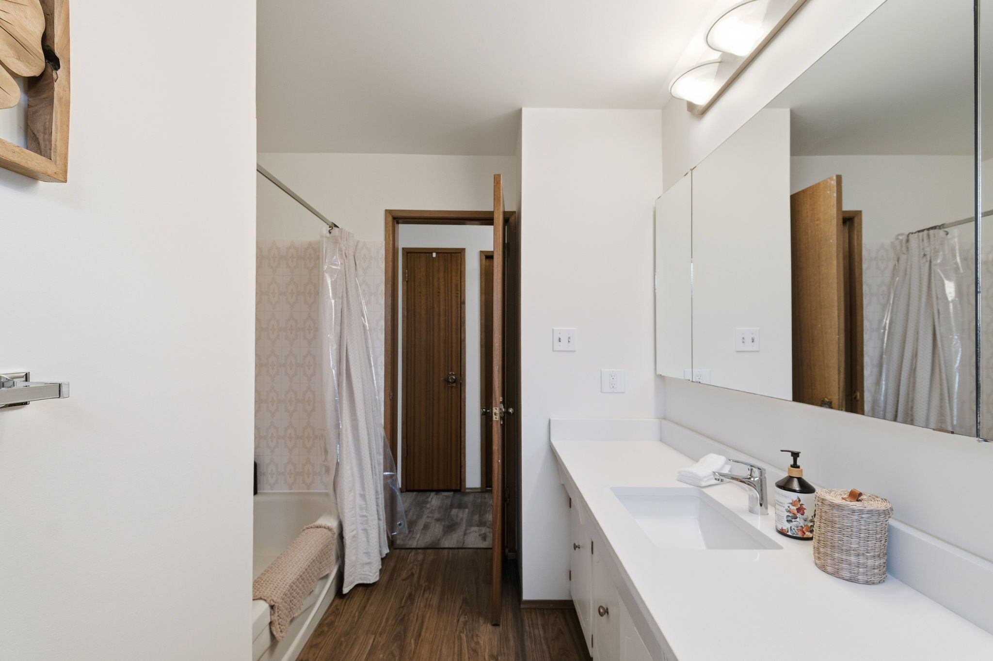 A modern bathroom with a large mirror, a white sink, and a shower area.