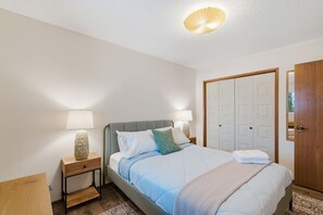 A neatly arranged bedroom with a bed, bedside tables, a nightstand, a wardrobe, and a mirror. - Mill - Cozy Main Floor Suite Near Whyte & Ravine (Edmonton)