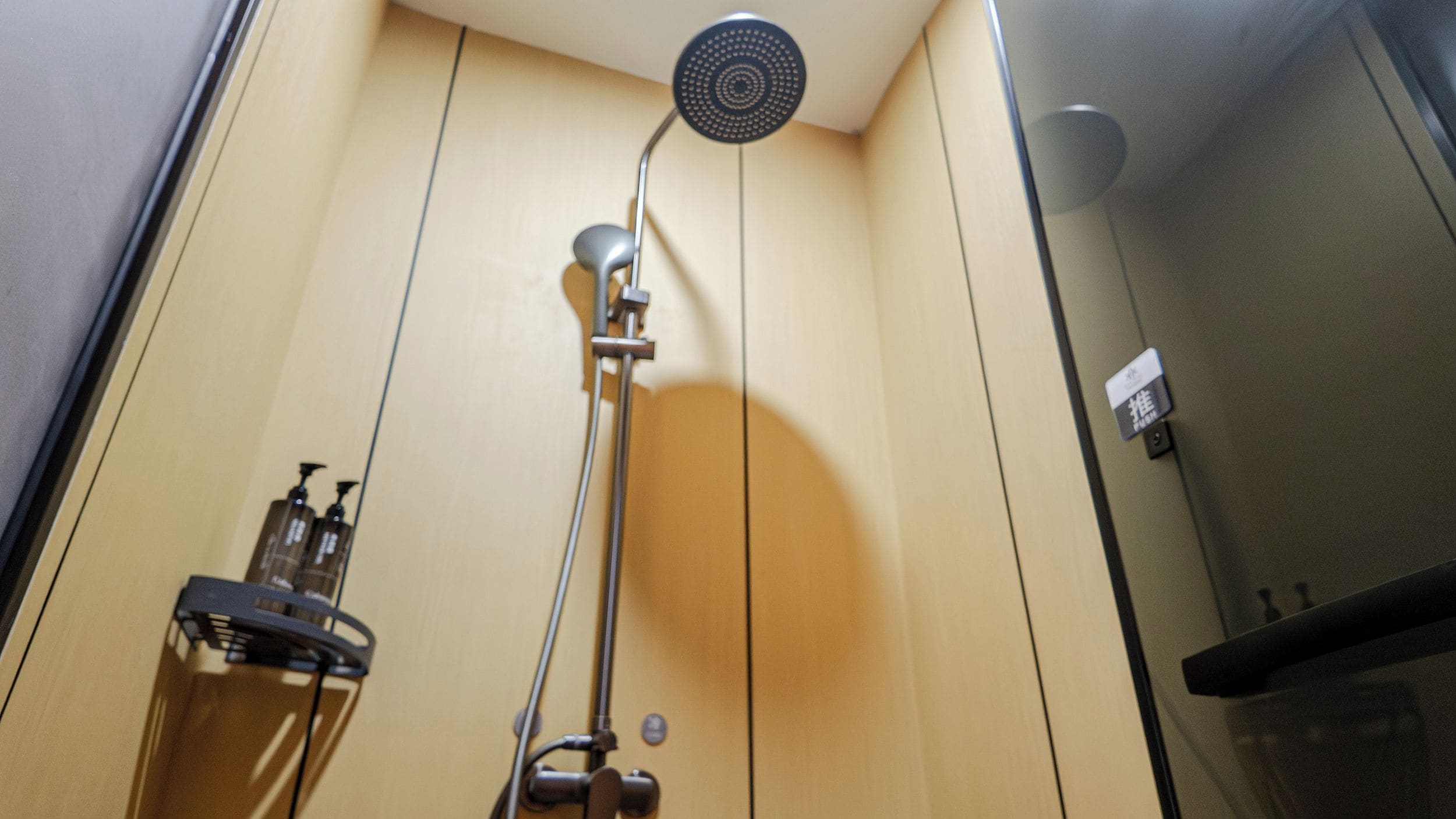 A shower with a handheld showerhead, a wall-mounted faucet, and a soap dispenser on a shelf.