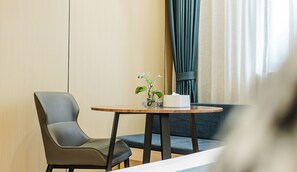 Una camera d'albergo con un tavolino rotondo, una sedia, un piccolo vaso con una pianta e un astuccio per fazzoletti.