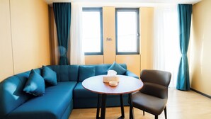 A modern living room with a blue sectional sofa, a round wooden table, and a brown armchair. - Ellie Hotel (Phnom Penh)