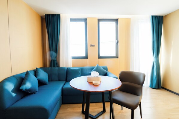 A modern living room with a blue sectional sofa, a round wooden table, and a brown armchair. - Ellie Hotel (Phnom Penh)