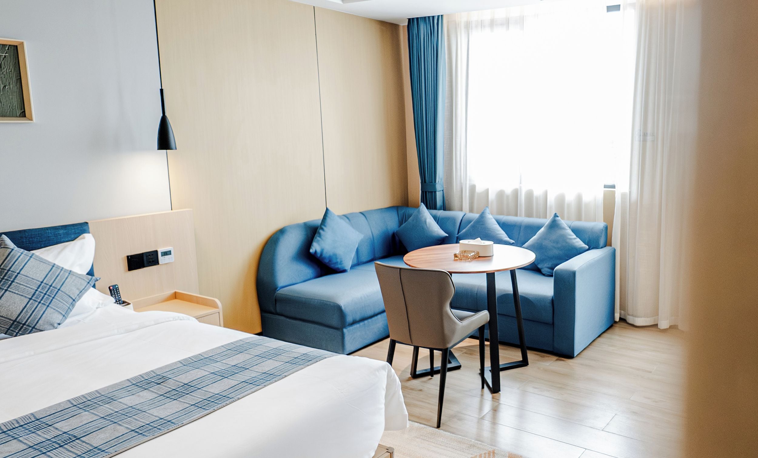 Een hotelkamer met een bed, een slaapbank, een stoel, een klein tafeltje en een raam met gordijnen.