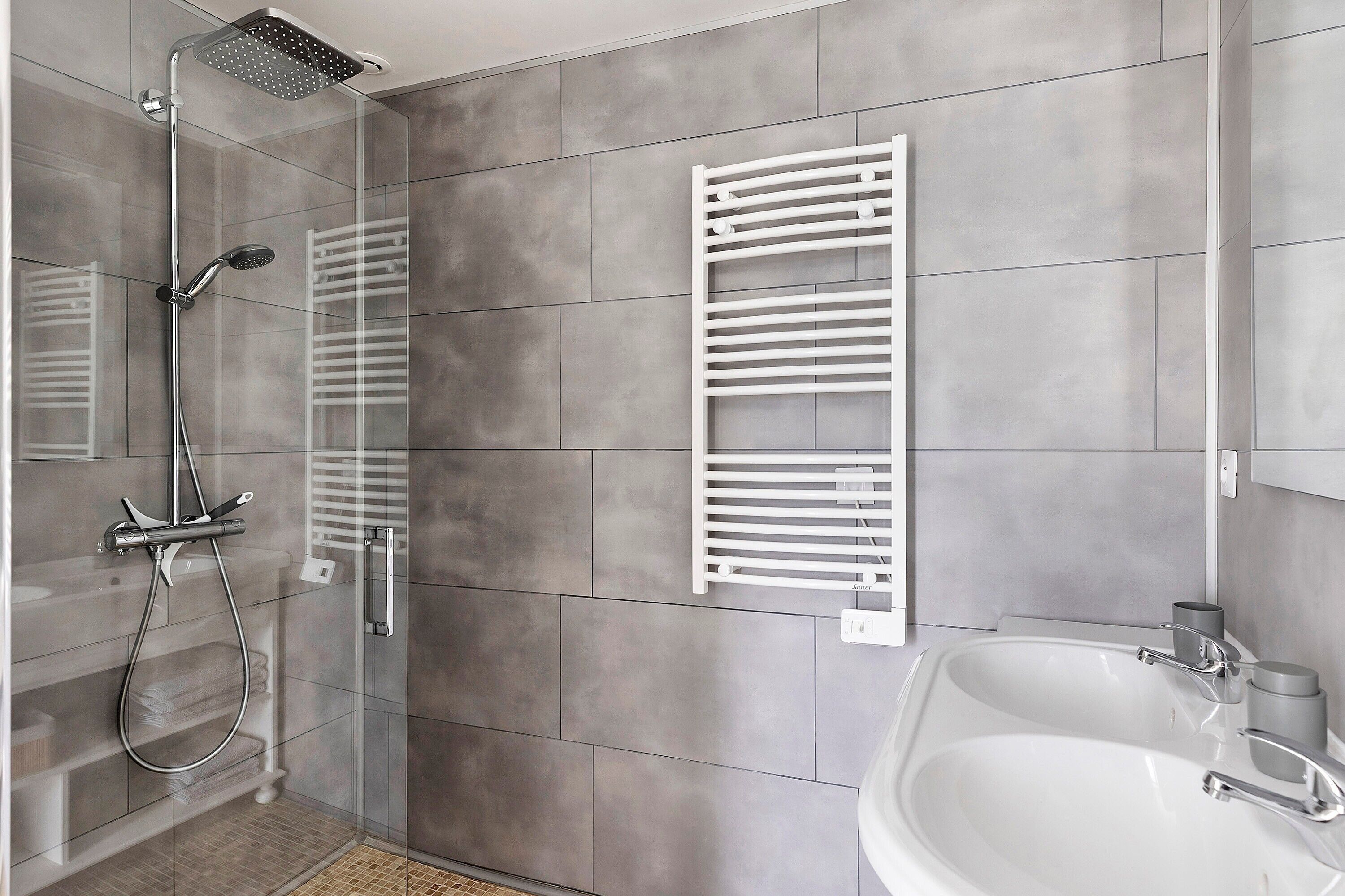 Un baño moderno con ducha, un lavabo blanco y un perchero para toallas.