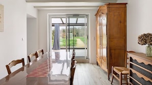 A dining area with a long table, chairs, a wooden cabinet, and a view through a glass door.