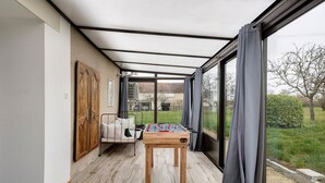 A room with a foosball table, a sofa, and a large window with curtains.
