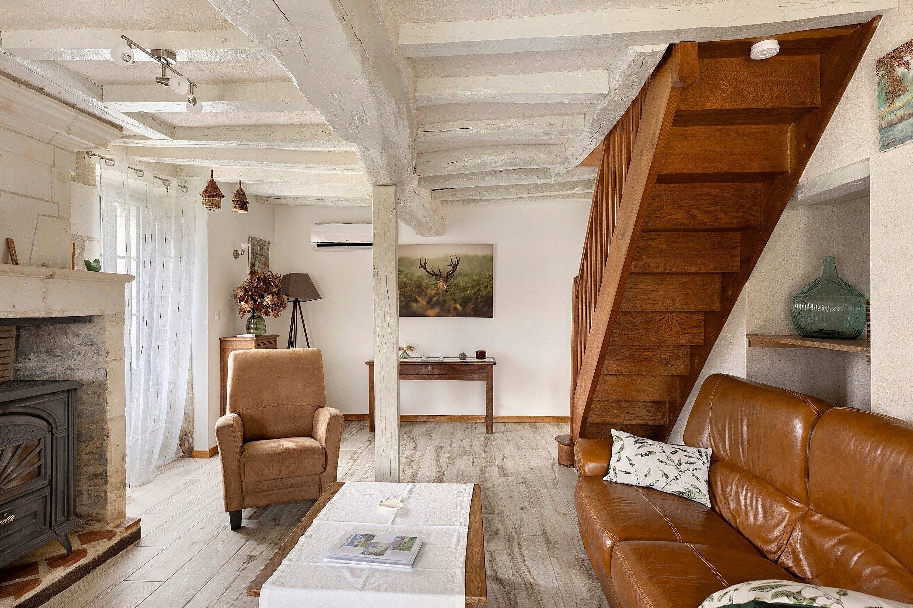 Uma sala de estar com lareira, um sofá de couro marrom, uma mesa de centro de madeira, uma poltrona marrom e uma escada de madeira.