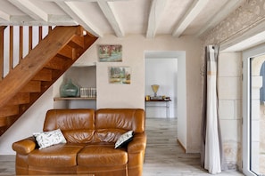 Ein braunes Ledersofa mit zwei Kissen, eine Holztreppe und zwei Bilder an der Wand.