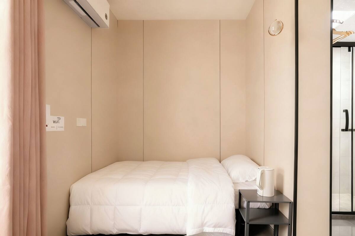 Habitación de hotel minimalista con cama, mesita de noche y hervidor.
