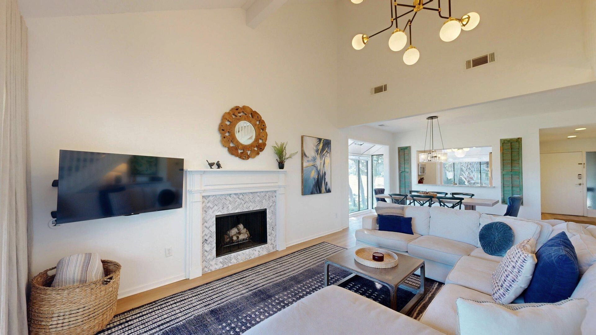 Amplia sala de estar con chimenea, un televisor de pantalla plana grande, comedor con mesa y sillas, y una lámpara moderna.