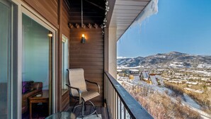 Un balcon en bois avec une chaise et une table, donnant sur un paysage enneigé parsemé de bâtiments.