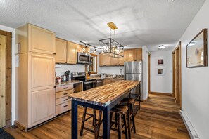 A modern kitchen with wooden cabinets, stainless steel appliances, and a central island with stools. - Ski Week Basecamp | Fireside Nights & Ski Shuttle (Steamboat Springs)
