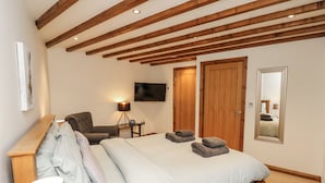 Quarto com cama grande, vigas de madeira no teto, televisão, cadeira e espelho.