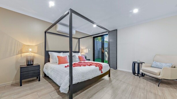 A modern bedroom with a four-poster bed, a nightstand, a chair, and a small table.