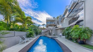 A modern building with a swimming pool, surrounded by palm trees and potted plants.