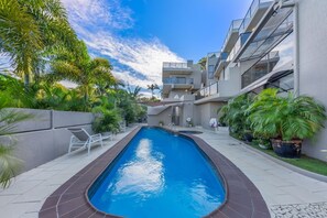A modern building with a swimming pool, surrounded by palm trees and potted plants.