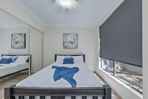 A bedroom with a bed, a window with a view, and artwork on the wall. - Island Vista Penthouse (Airlie Beach)