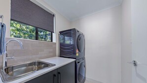 A compact kitchen with a sink, a window with a view of trees, and a stacked washer and dryer.