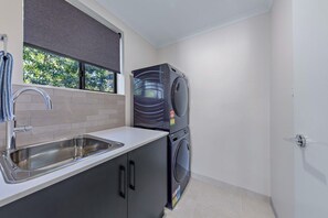 A compact kitchen with a sink, a window with a view of trees, and a stacked washer and dryer.