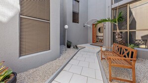 A pathway leading to a wooden bench and a door, with a small garden area and a potted plant.