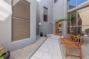 A pathway leading to a wooden bench and a door, with a small garden area and a potted plant.