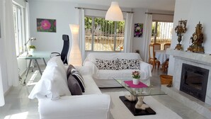 Ein Wohnzimmer mit einem weißen Sofa, einem Glastisch, einem Kamin und einem Essbereich mit Stühlen und Tisch.